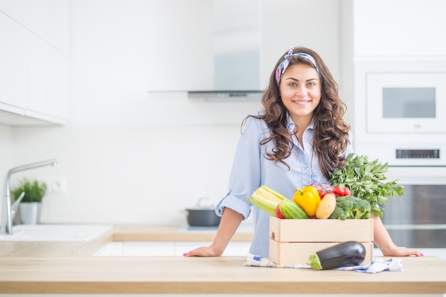 Femme dans sa cuisine avec une boîte en bois pleine de légumes biologiques.