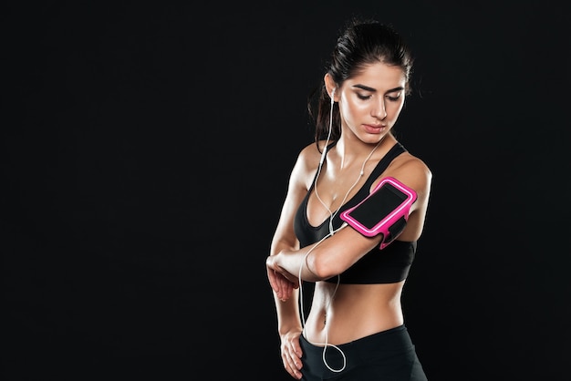 femme dans une salle de sport debout sur un mur noir regardant de côté tout en écoutant de la musique avec des écouteurs