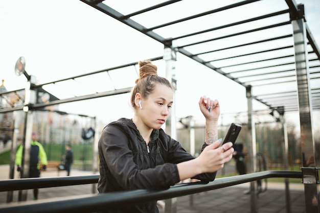 Femme dans une salle de sport en plein air avec un casque et un smartphone.