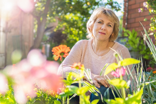 Une femme dans son jardin s'occupe des fleurs et des plantes par une journée ensoleillée.