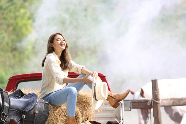 une femme dans un style cowgirl est assise dans un ranch de chevaux avec un environnement agricole occidental.