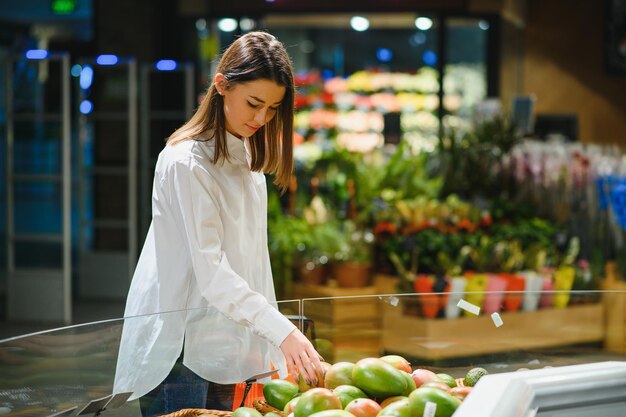 Femme dans un supermarché à l'étagère de légumes faisant l'épicerie, elle choisit