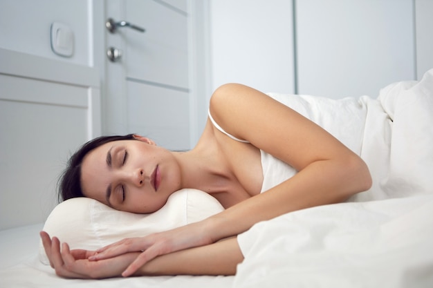 Femme dans un t-shirt blanc est allongée sur le lit et un oreiller est sous la couverture dans la chambre