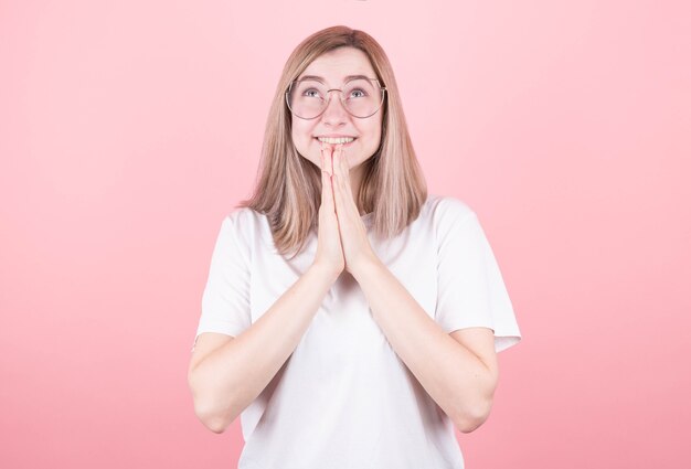 Femme dans un t-shirt blanc fait un vœu pour un anniversaire sur un mur rose.