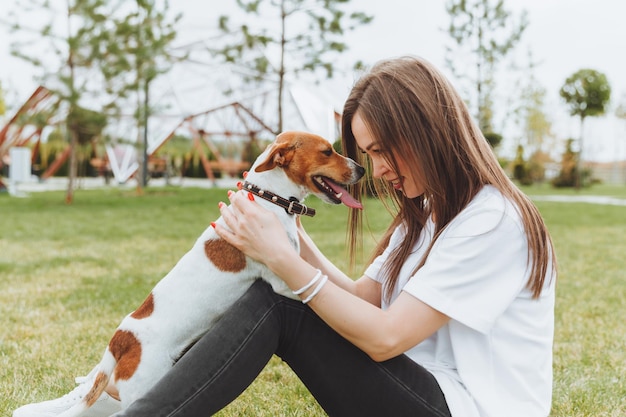 Une femme dans un t-shirt blanc et un jean embrasse son chien Jack Russell Terrier dans la nature dans le parc Meilleurs amis fidèles depuis l'enfance