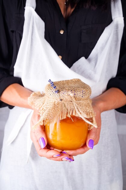 Une femme dans un tablier blanc tient un pot de miel