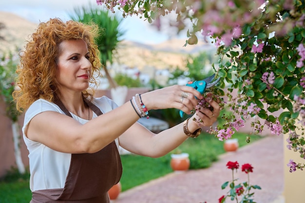 Femme dans un tablier avec buisson fleuri sécateur dans le jardin