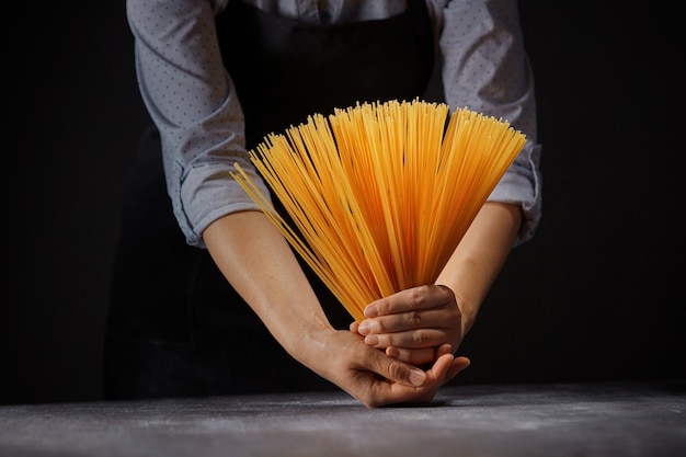 Femme dans un tablier tenant un tas de spaghettis crus