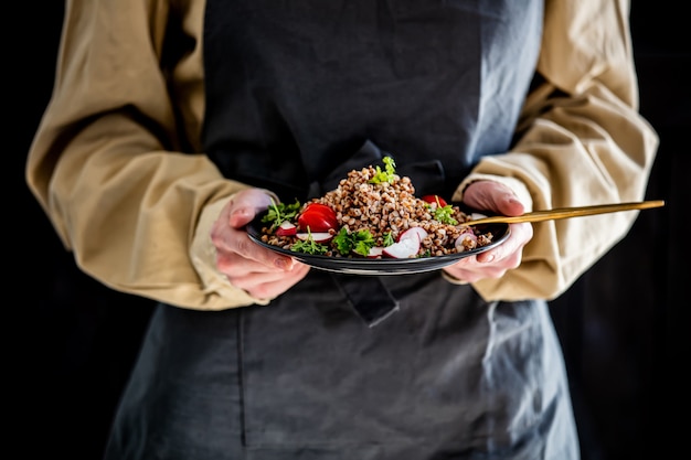 Femme dans un tablier tient une assiette de sarrasin dans ses mains