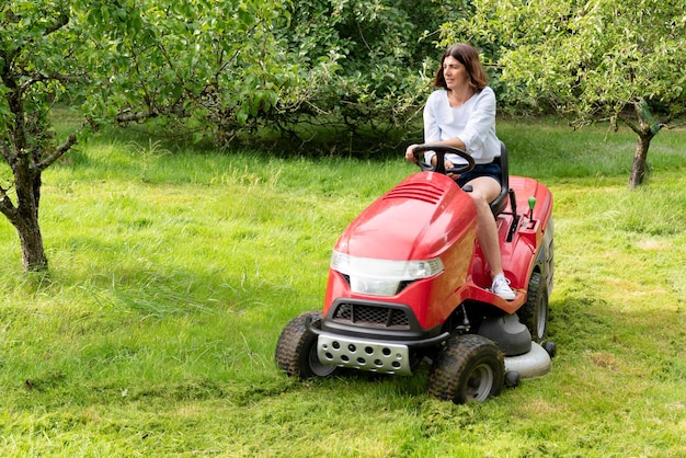 Femme dans un travail de jardin sur le terrain au volant d'une tondeuse à gazon