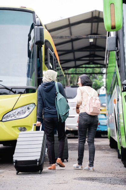 Une femme dans un voile avec un sac et une valise se dirige vers le bus tout en discutant avec une femme aux cheveux courts en allant en bus