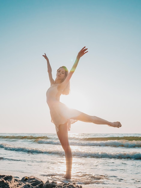 Femme dansant avec les bras levés sur la plage contre un ciel clair