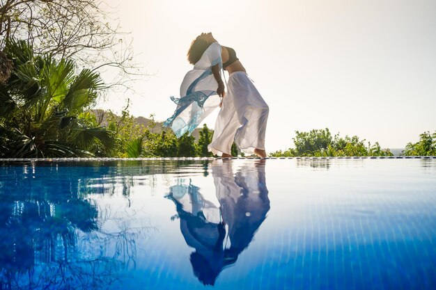 Femme dansant debout à côté d'une piscine tropicale extérieure