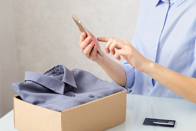 Une femme déballe une boîte en carton avec des vêtements, achète des marchandises en ligne, concept de livraison.