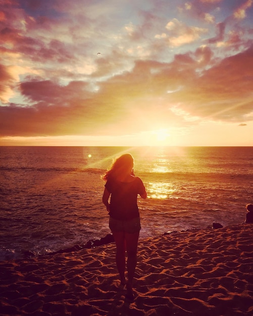 Photo une femme debout contre la mer au coucher du soleil.