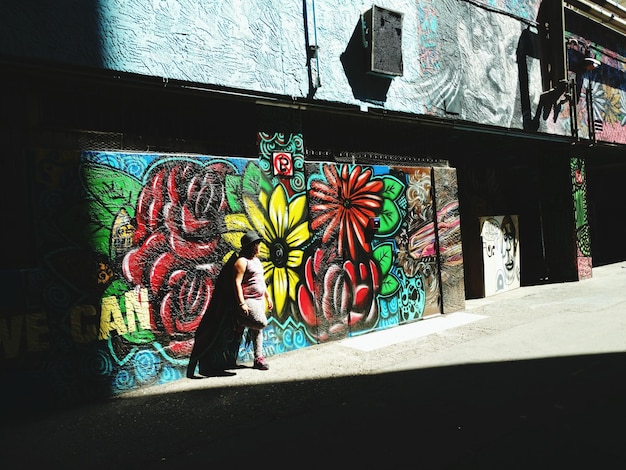Une femme debout contre un mur de graffitis pendant une journée ensoleillée
