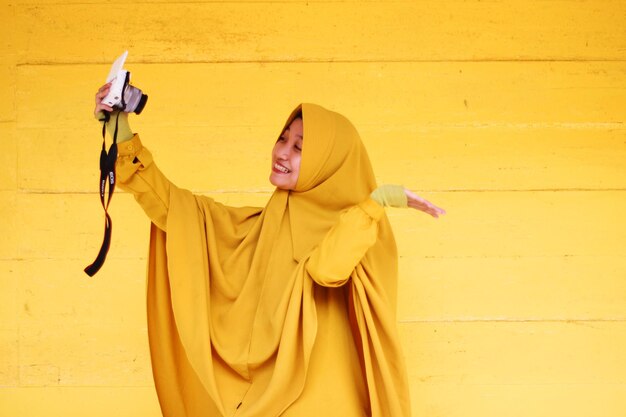 Photo une femme debout contre un mur jaune.