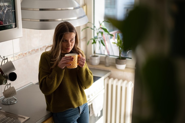 Femme debout dans la cuisine et boire une tasse de thé