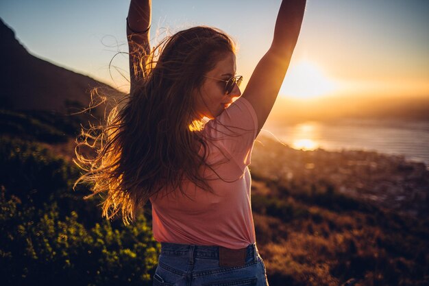 Photo une femme debout face à la mer au coucher du soleil