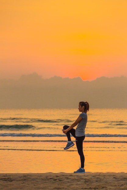 Femme debout et faire de l'exercice sur la plage le matin avec un ciel coloré et une vague en arrière-plan.