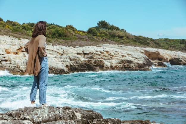 Femme debout sur la falaise profitant de la vue sur la mer par temps venteux journée ensoleillée