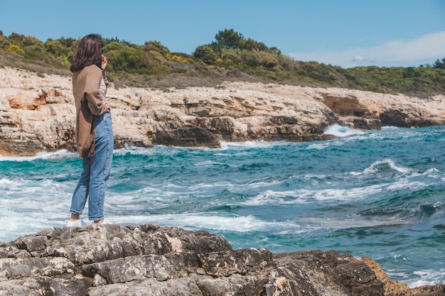 Femme debout sur la falaise profitant de la vue sur la mer par temps venteux journée ensoleillée