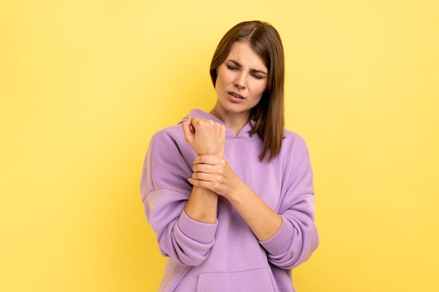 Femme debout avec une grimace de douleur massant le poignet douloureux souffrant d'une blessure à la main ou d'une entorse