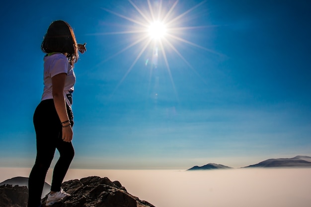 Photo femme debout pointant vers le soleil sur un fond de montagne une mer de nuages