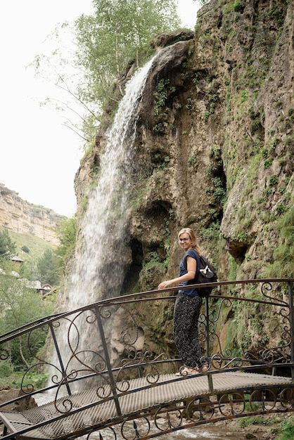 Femme debout sur le pont en regardant la belle cascade de montagne