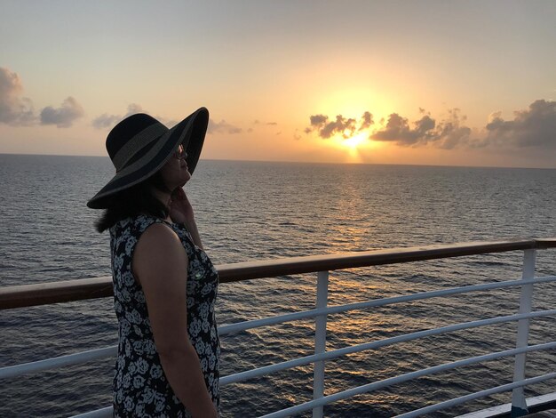 Femme debout près de la balustrade contre le ciel au coucher du soleil