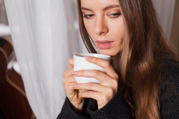 Femme debout près de la fenêtre et boire du café