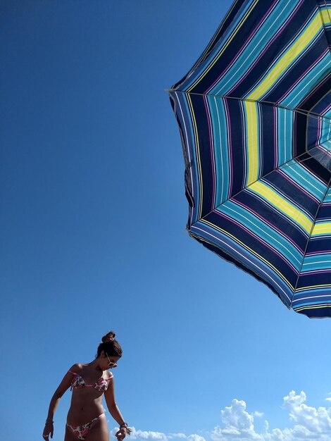 Une femme debout près d'un parapluie contre le ciel bleu