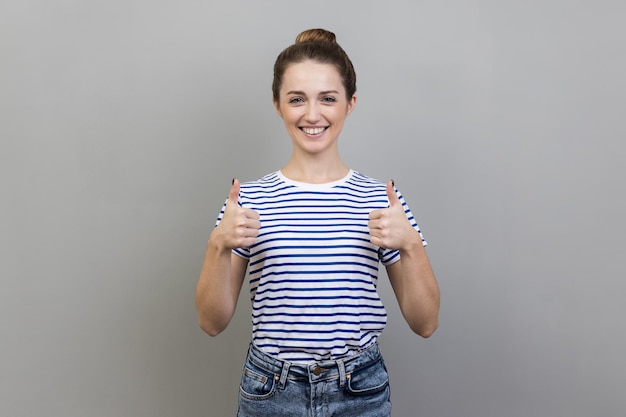 Femme debout et regardant la caméra avec un sourire à pleines dents montrant le pouce vers le haut comme un geste