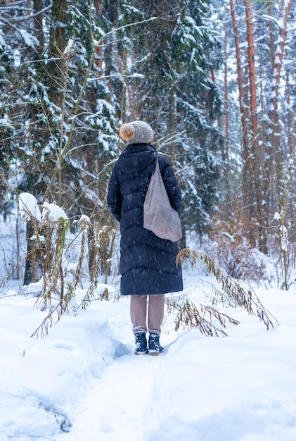 Femme debout son dos dans la forêt d'hiver pendant la promenade de vacances à pied dans les bois seul avec sac fourre-tout en bonnet tricoté