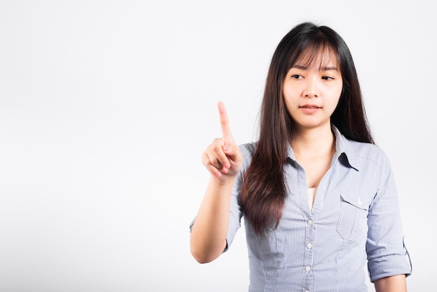 Femme debout son sourire confiant en touchant un écran imaginaire avec son doigt isolé sur fond blanc, portrait asiatique heureux belle jeune femme appuyant sur le bouton en studio tourné