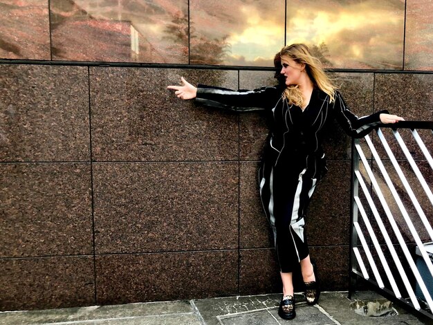 Une femme debout sur le trottoir contre le mur.