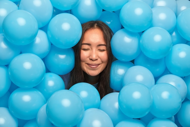 femme debout avec les yeux fermés sort la tête à travers des ballons gonflés bleus