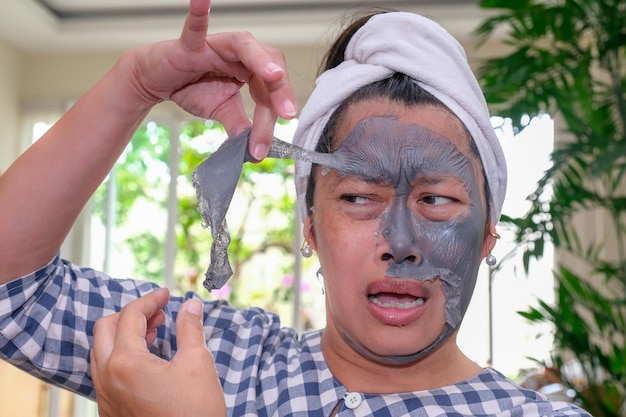 Une femme décollant un masque facial de beauté sur son visage avec une expression paniquée