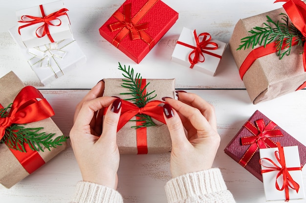 La femme décore la boîte-cadeau avec un ruban rouge. Emballage des cadeaux de Noël.