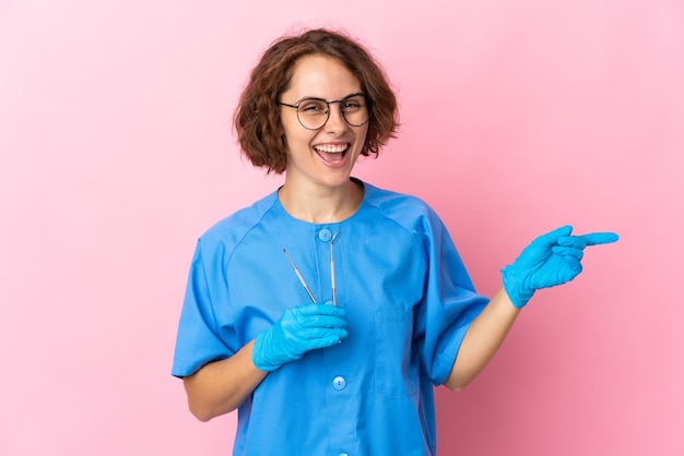 Femme dentiste anglais tenant des outils sur le doigt pointé rose sur le côté