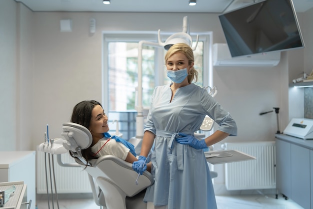 Femme dentiste en clinique dentaire fournissant un examen et un traitement de la cavité buccale pour le patient.