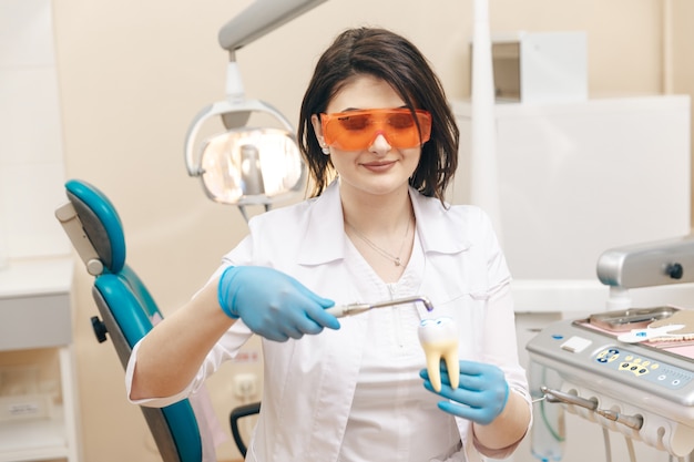 Femme dentiste dans le masque montrant comment faire le limage des dents sur le modèle de la dent.