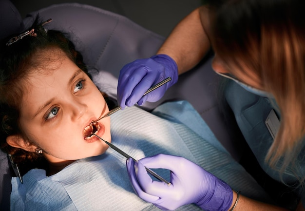Femme dentiste examinant les dents d'une petite fille dans un cabinet dentaire