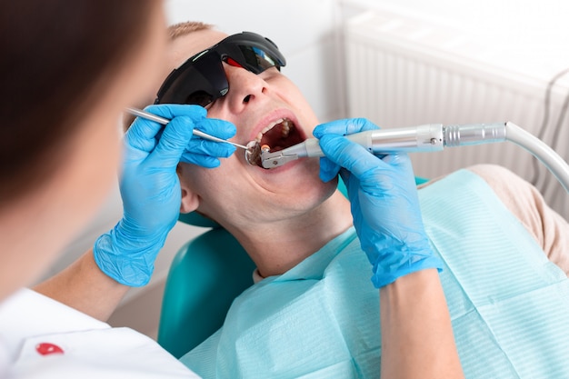 Une femme dentiste examine la cavité buccale du patient avec un outil avec un miroir. Portrait en gros plan d'un patient avec la bouche ouverte, un médecin en gants est titulaire d'un miroir dentaire.