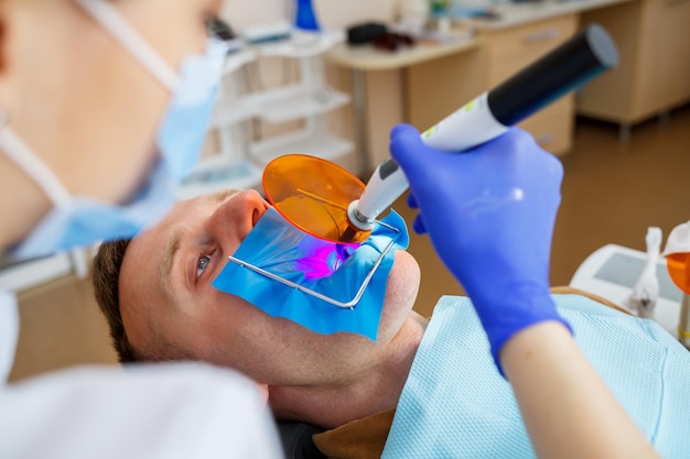 Une femme dentiste examine le patient avec des instruments dans la clinique dentaire. Le médecin fait un traitement dentaire sur les dents d'une personne dans le fauteuil du dentiste. Mise au point sélective