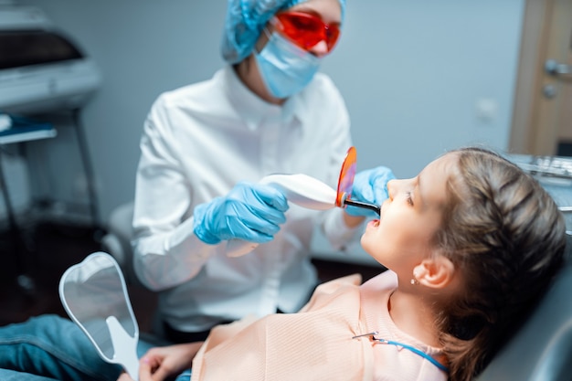 Femme dentiste fournissant une restauration dentaire et un remplissage avec une lampe UV de polymérisation pour enfant