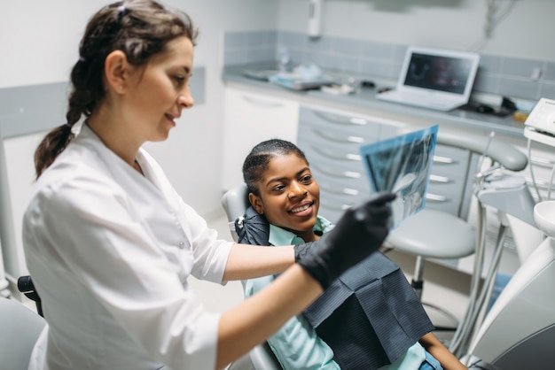 Photo femme dentiste montre une image radiographique au patient, clinique dentaire. femme en cabinet dentaire, stomatologie, soins des dents