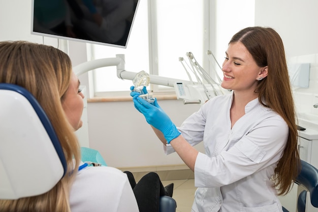 Une femme dentiste montre à une jeune fille un modèle de mâchoire artificielleLe dentiste montre comment bien prendre soin de la cavité buccale le coût et les conséquences