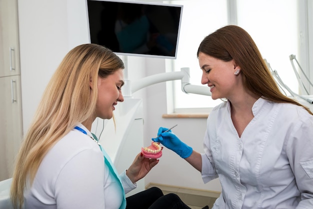 Une femme dentiste montre à une jeune fille un modèle de mâchoire artificielleLe dentiste montre comment bien prendre soin de la cavité buccale le coût et les conséquences