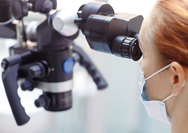 Femme dentiste avec des outils dentaires - microscope, miroir et sonde traitant les dents des patients au bureau de la clinique dentaire. Concept de médecine, de dentisterie et de soins de santé. Matériel dentaire